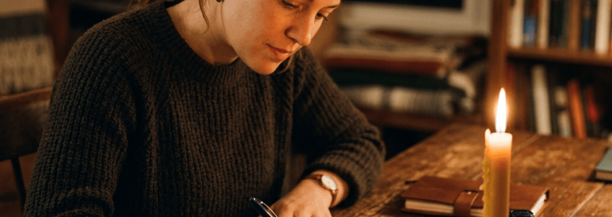 Woman writing a letter by candlelight at a wooden table