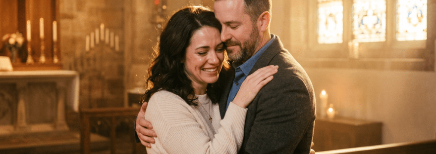 A man and woman hugging affectionately inside a church near stained glass windows.